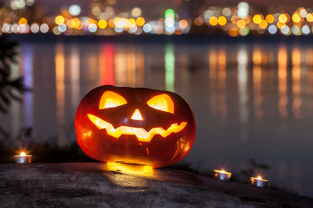 halloween pumpkin on a log at the background of night city with reflection lights on the water