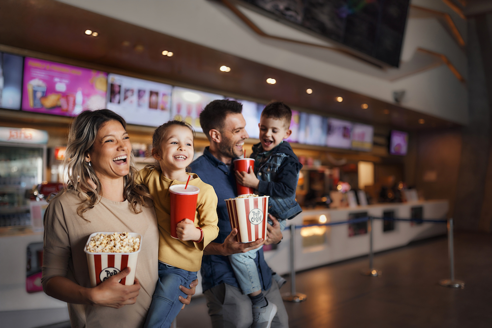 Happy family enjoying while walking with popcorn and drinks in cinema.